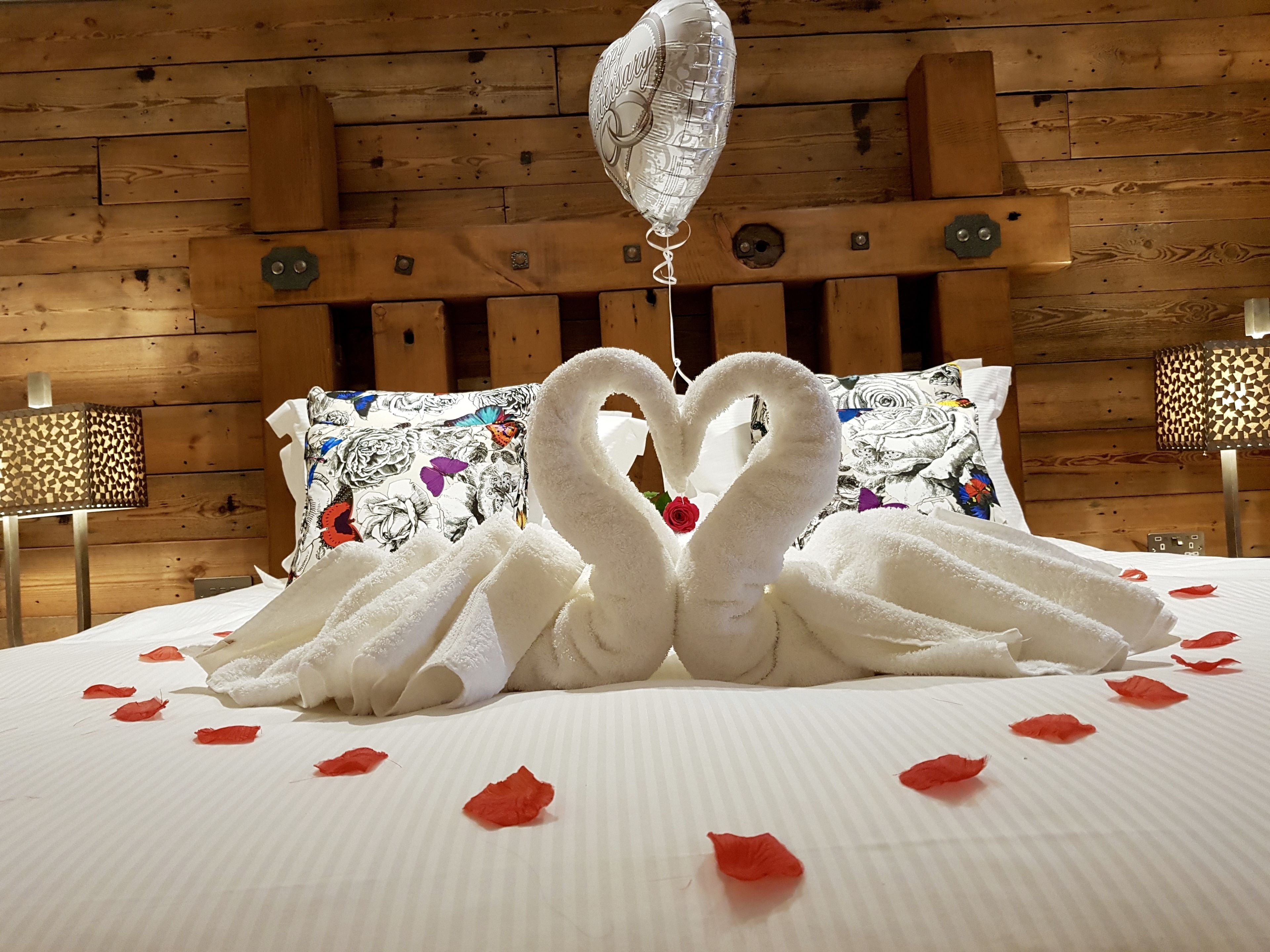 A bed with towels arranged in the shape of swans, a balloon, and rose petals on the bed.
