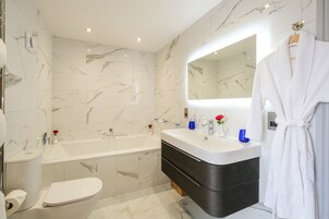 Un baño moderno con piso de mármol, una bañera blanca, un tocador con espejo y una bata blanca colgada en la pared.