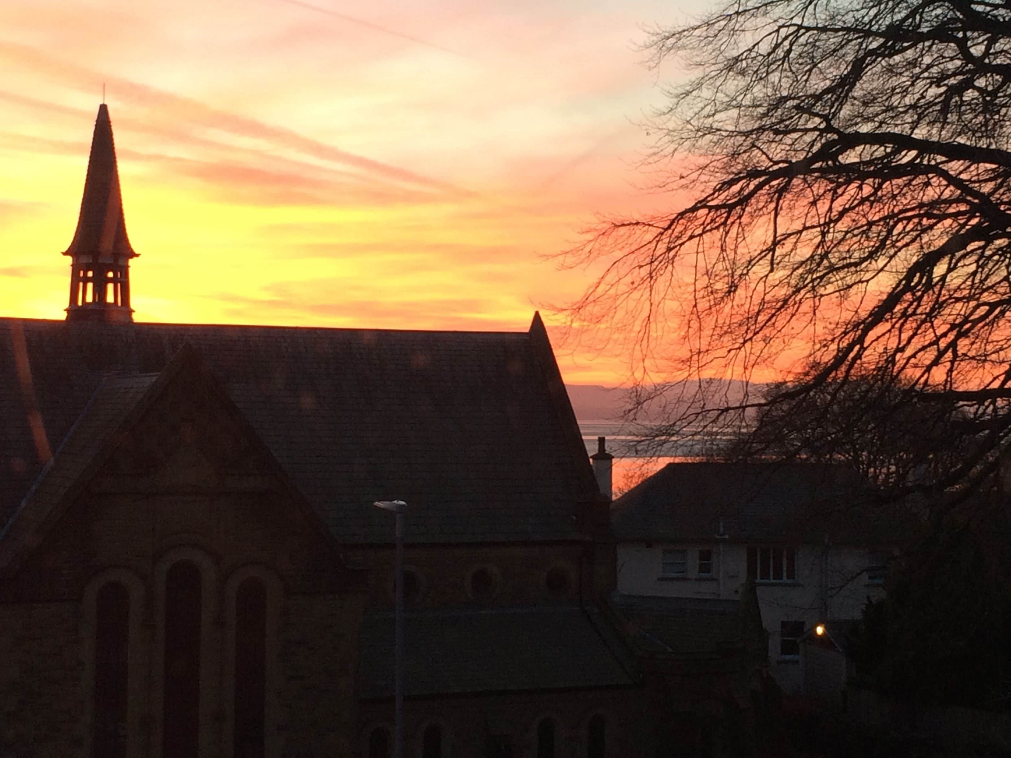 A church with a prominent steeple and arched windows, set against a sunset sky.