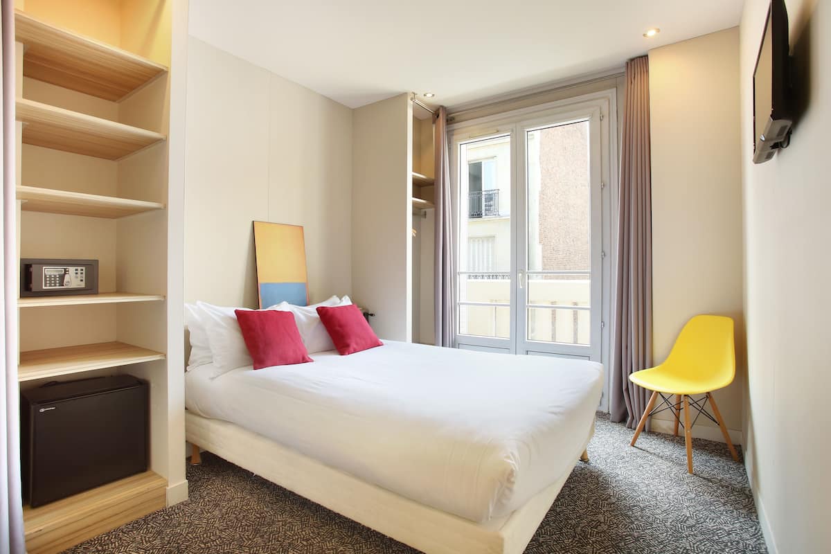 A hotel room with a bed, a desk, a chair, and a window with curtains.