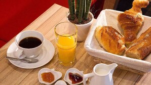 A breakfast setting with a cup of coffee, a glass of orange juice, pastries, and jam. - Hotel Auguste (Paris)