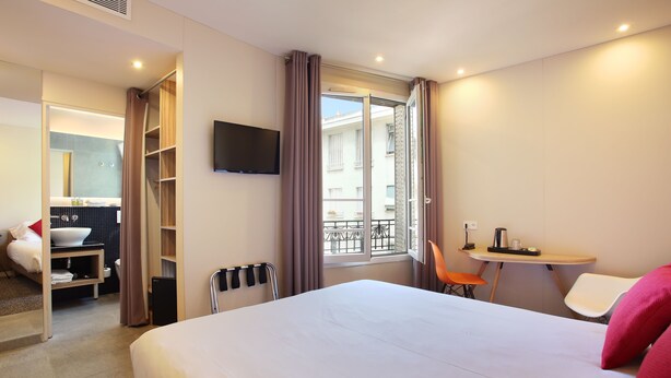 A hotel room with a large bed, a desk with a chair, a TV mounted on the wall, and a balcony with a view. - Hotel Auguste (Paris)