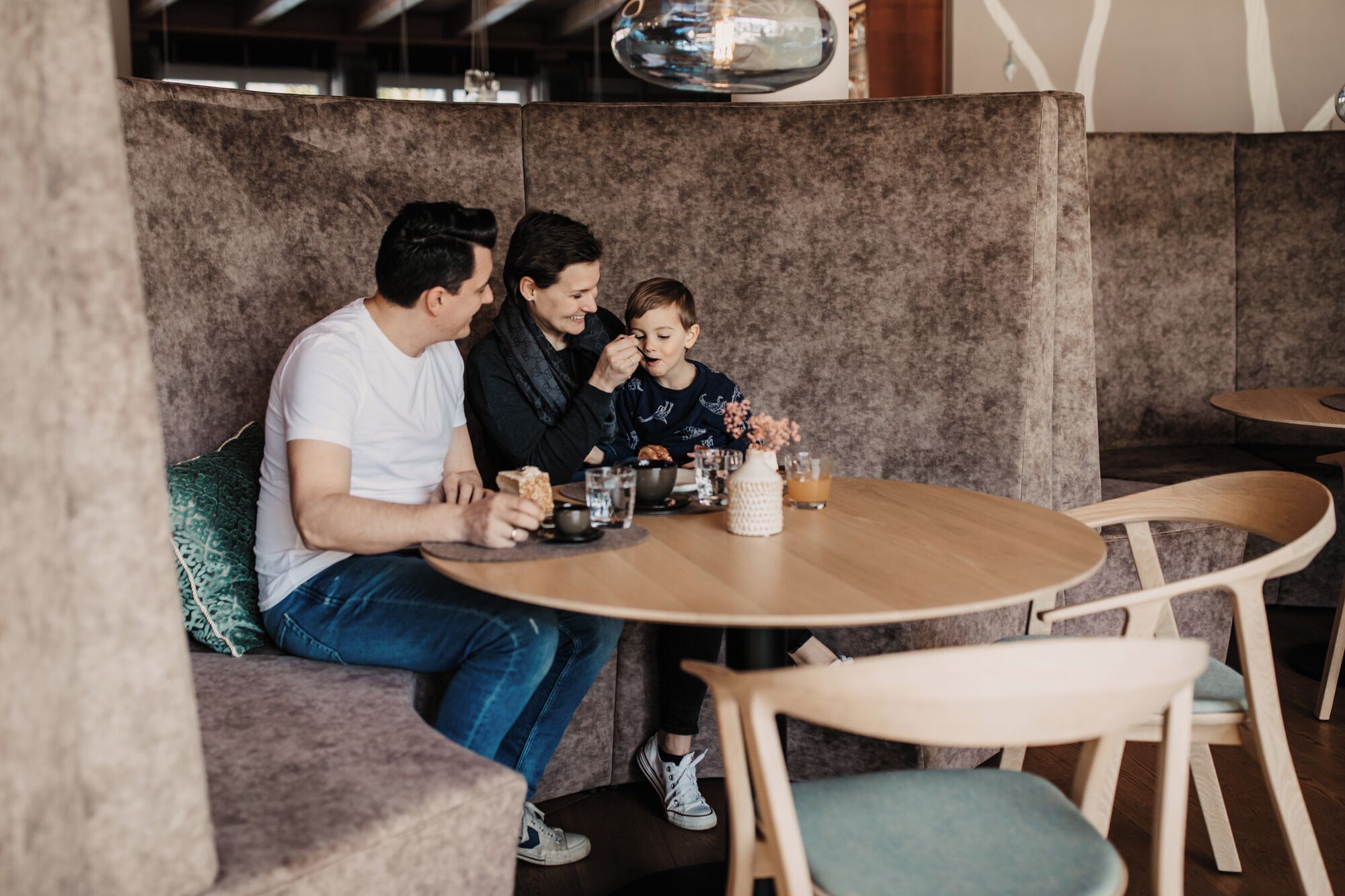 A family dining at a booth with a round wooden table, cushioned seating, and a vase with flowers.