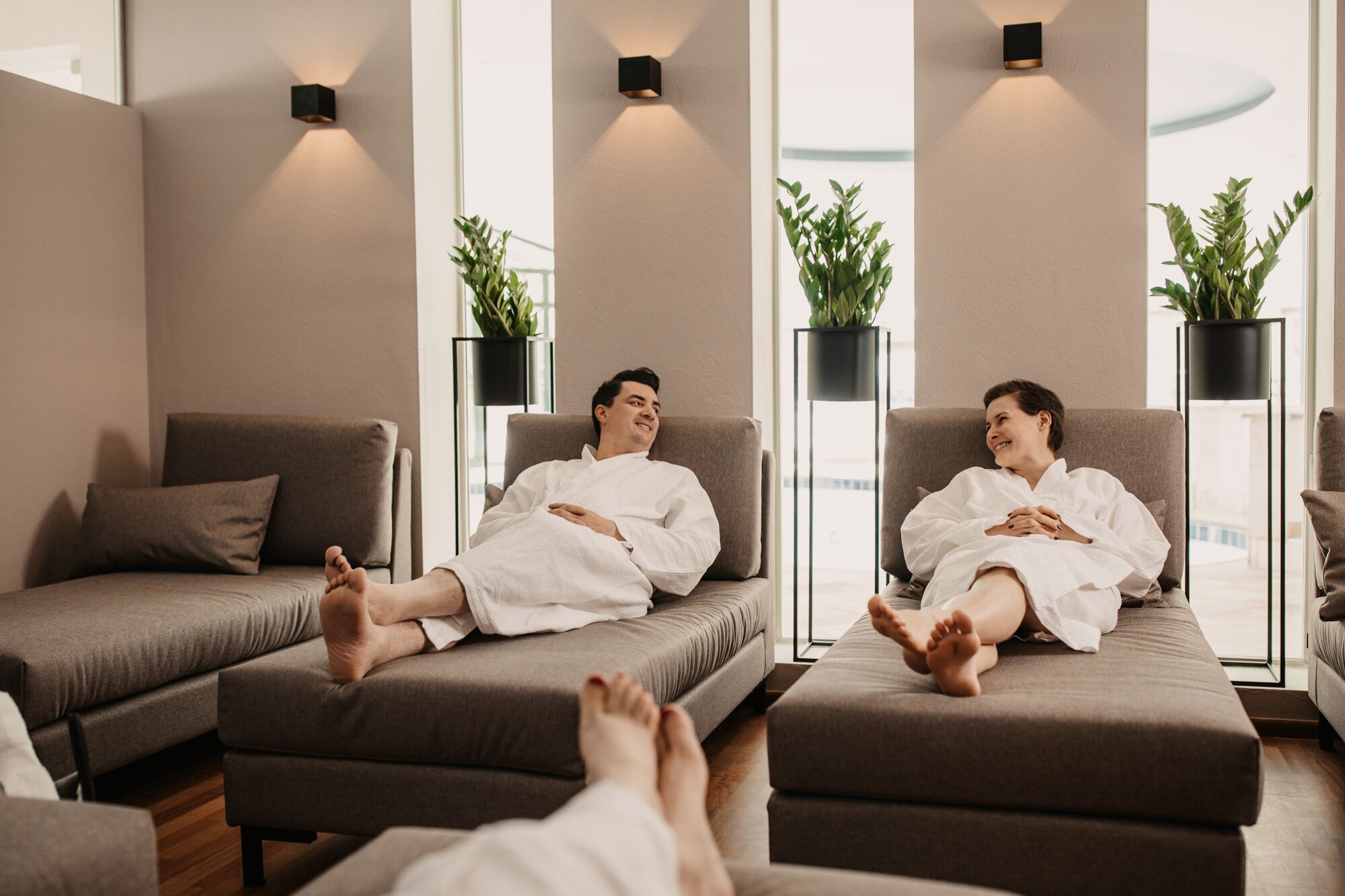 Une salle de spa moderne avec deux canapés, de grandes fenêtres et des plantes en pot.