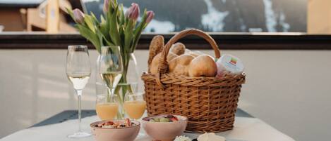 A table with a wicker basket containing bread, a bowl of fruit, and a glass of white wine.