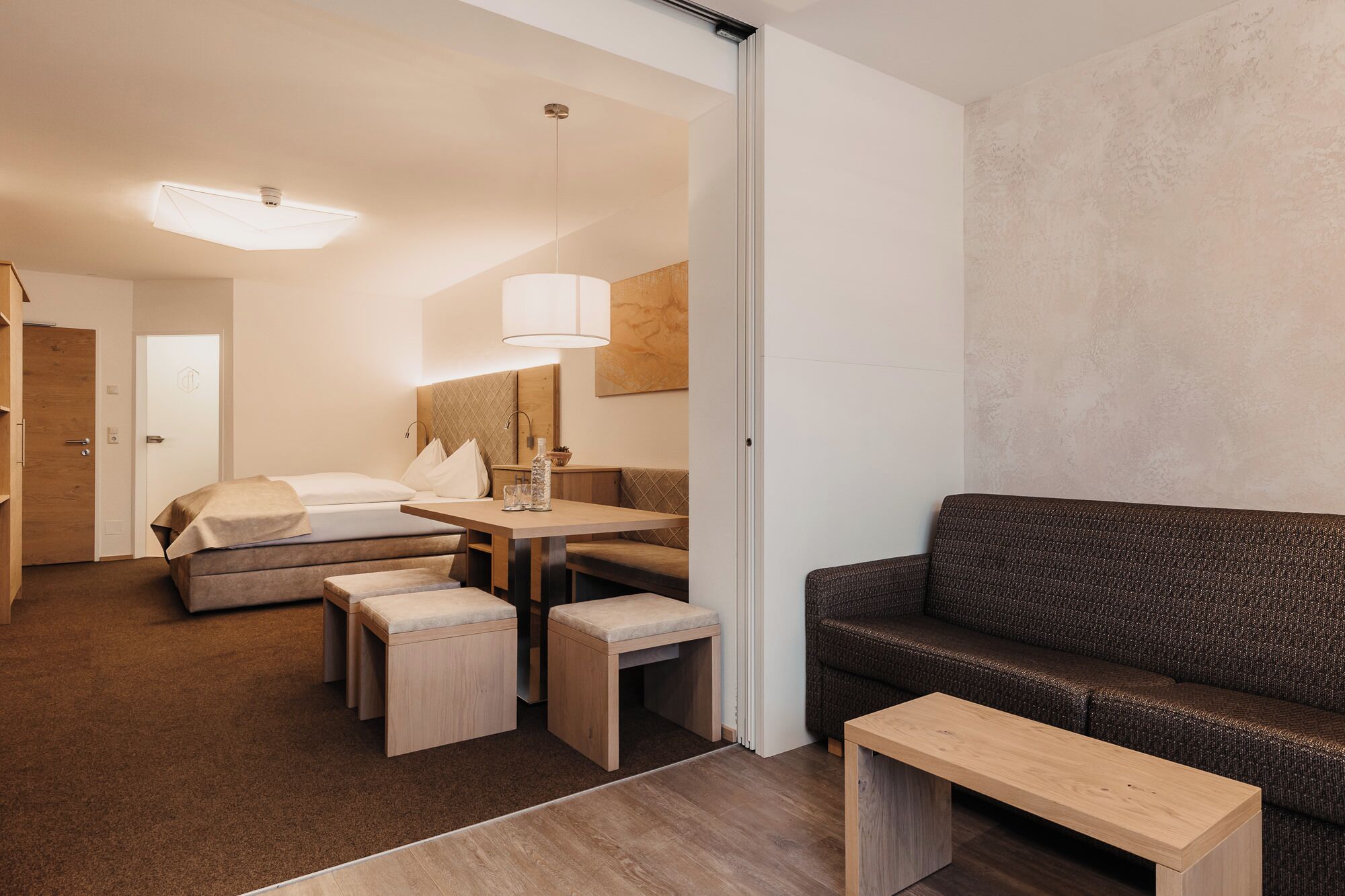 Ein modernes Hotelzimmer mit einem Bett, einer Couch, einem Esstisch mit Stühlen und einem kleinen Holztisch.