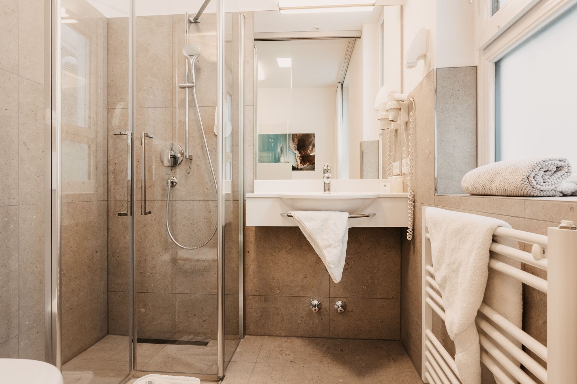 Ein modernes Badezimmer mit einer Duschkabine, einem Waschbecken mit Handtuchhalter und einem Spiegel darüber.