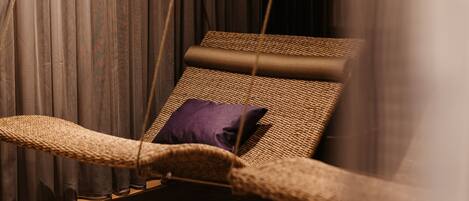 Una silla de mimbre con cojín morado, frente a cortinas oscuras.