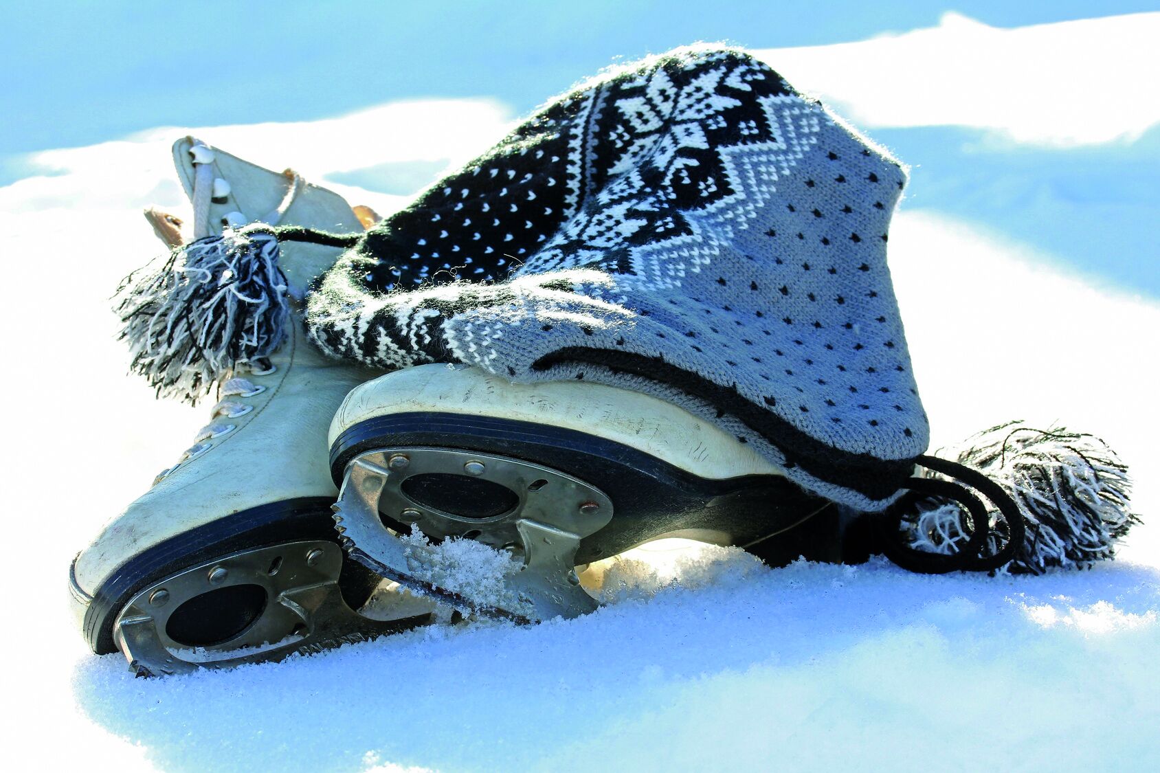 Un par de botas cubiertas de nieve y un gorro de punto con un diseño de copo de nieve, sobre la nieve.