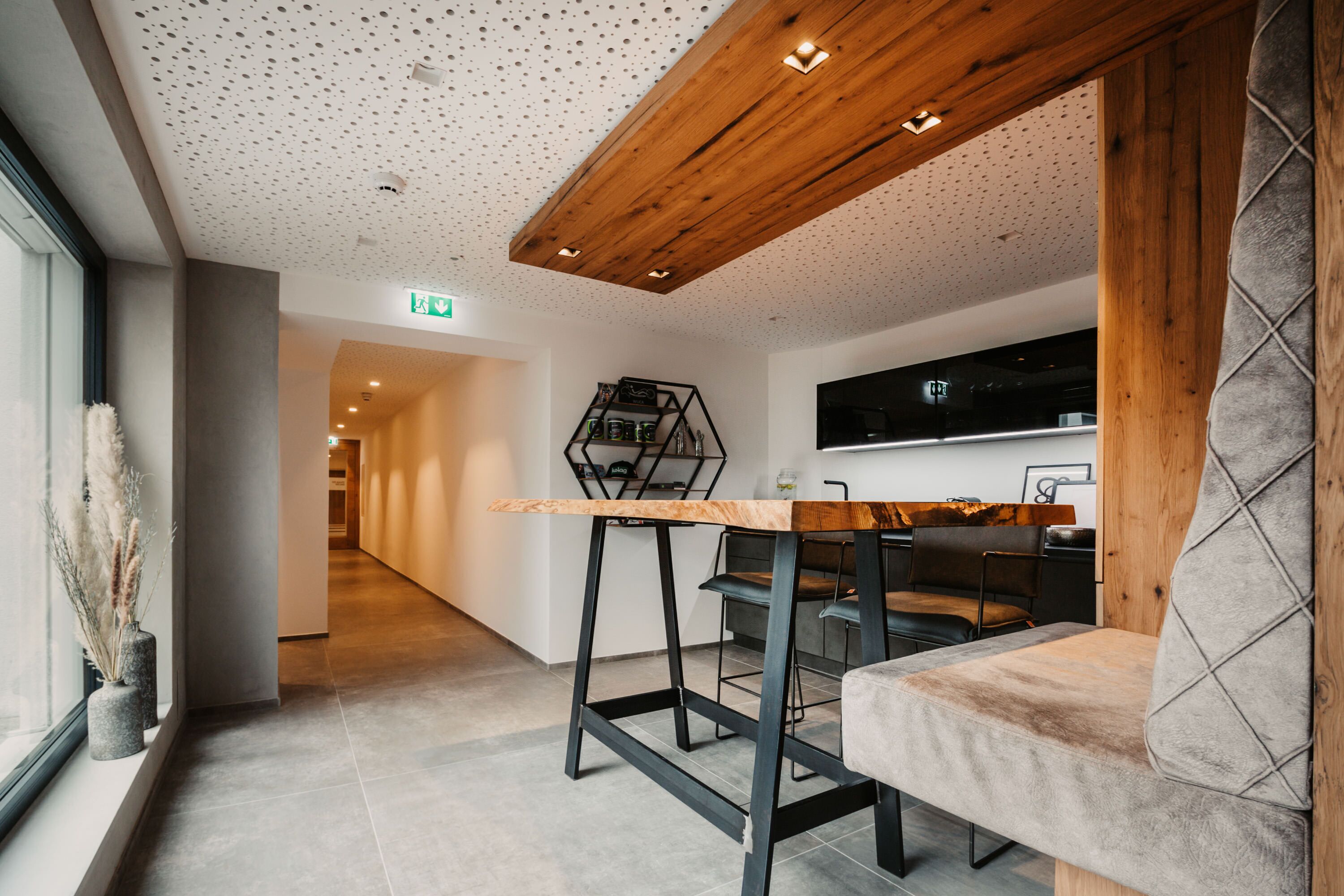 Un intérieur moderne avec un plafond en bois, un long couloir, un coin repas avec une table et des chaises en bois, et un téléviseur fixé au mur.