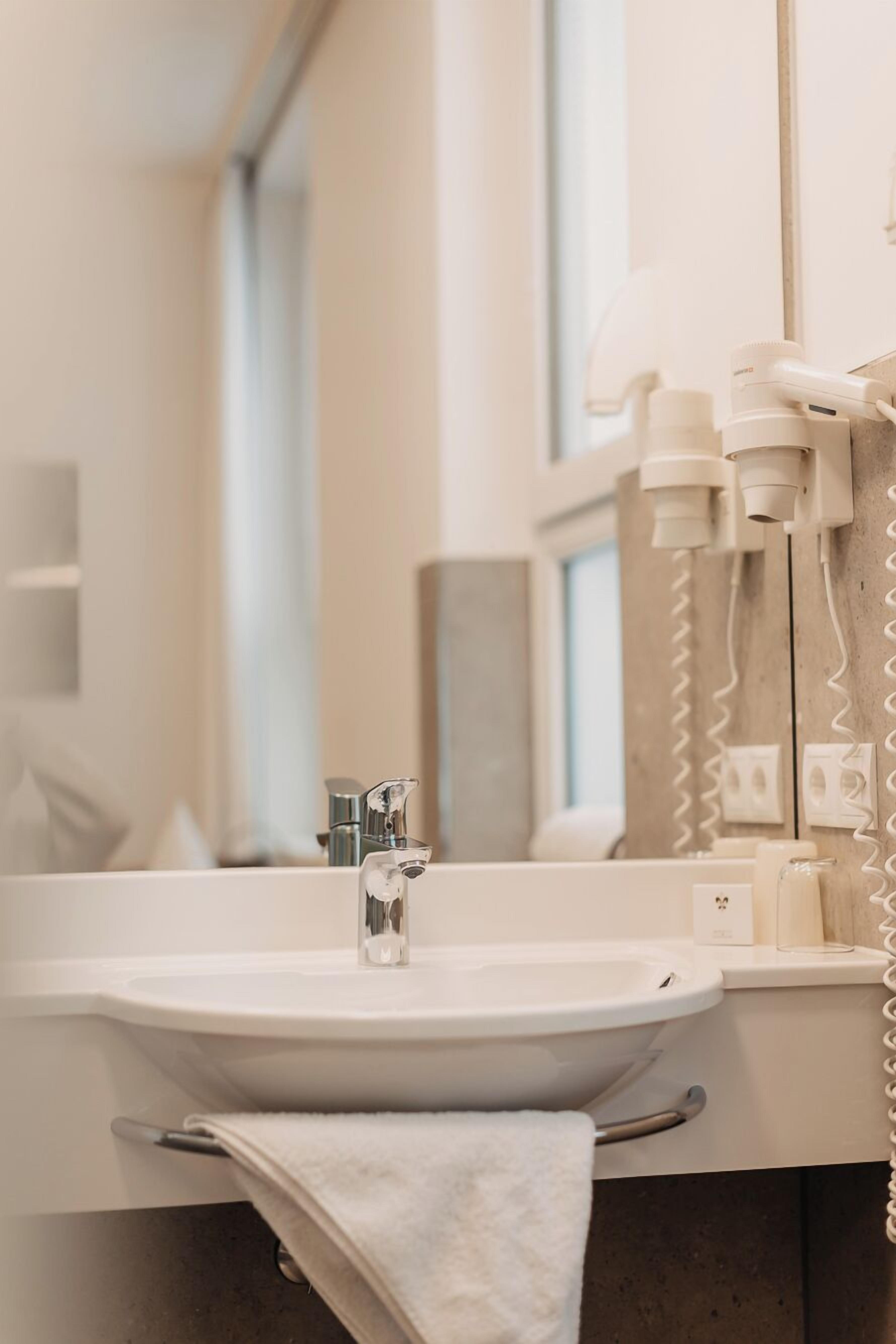 A modern bathroom with a white sink, a mirror, and a towel rack.