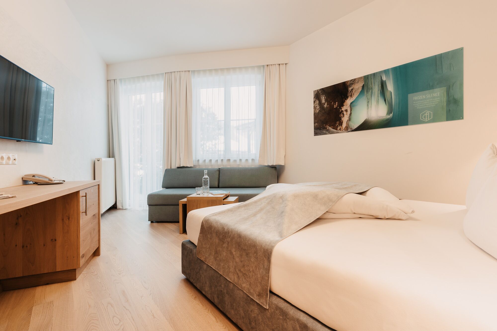 Una habitación de hotel moderna con cama, sofá, escritorio de madera y televisor.
