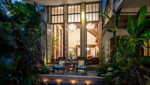 A well-lit outdoor seating area with chairs and tables, surrounded by lush greenery.