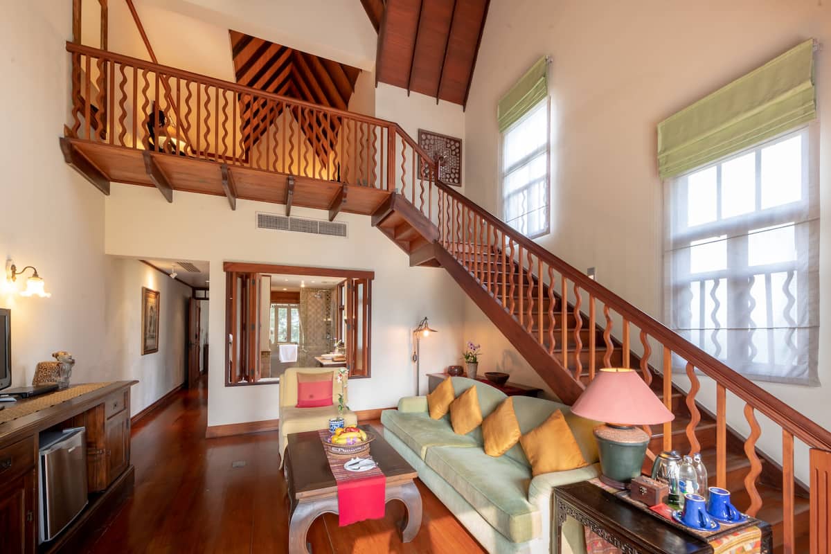 A spacious living area with a wooden staircase, a sofa, a coffee table, and a dining table.