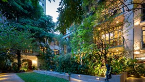 A courtyard with a central lawn, surrounded by buildings with illuminated windows, and a statue of a figure with a flower garland.