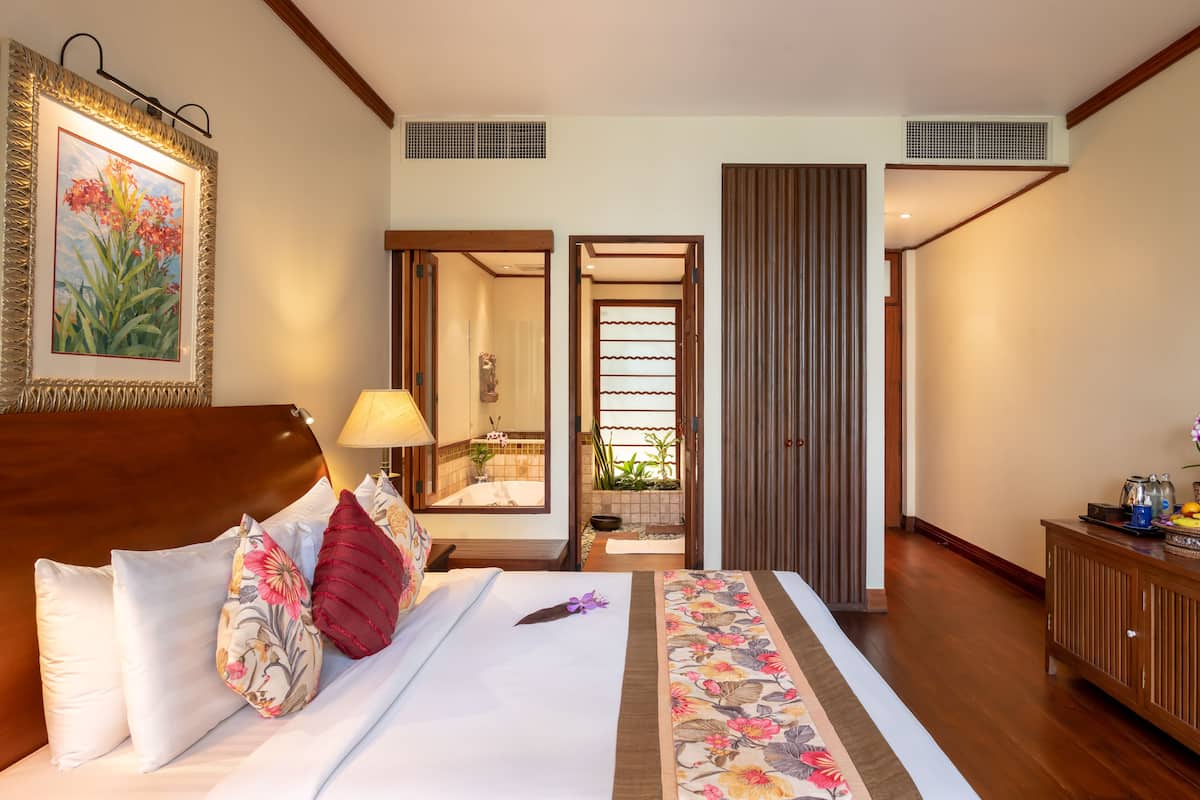 A hotel room with a bed, a nightstand, a lamp, a bathroom mirror, and a view of the bathroom.