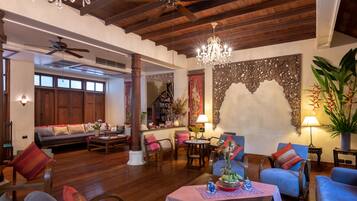 A spacious living area with wooden floors, a ceiling fan, a chandelier, and a large decorative wall piece.