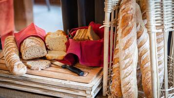 A variety of breads on a wooden cutting board, some in a wicker basket, and a red cloth nearby.