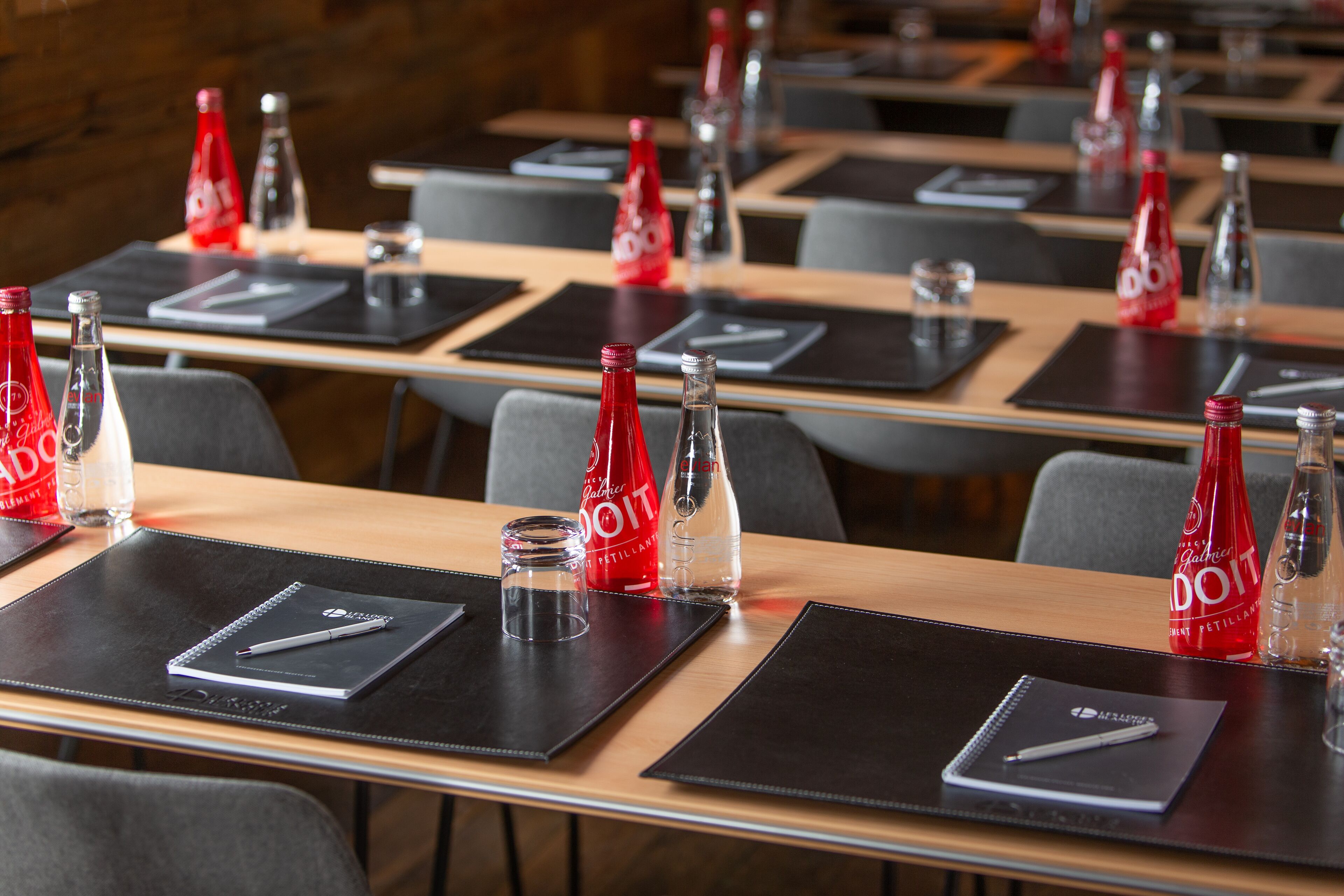 Un salón de conferencias con mesas dispuestas para reuniones, cada una con una libreta, un bolígrafo y una botella de agua.