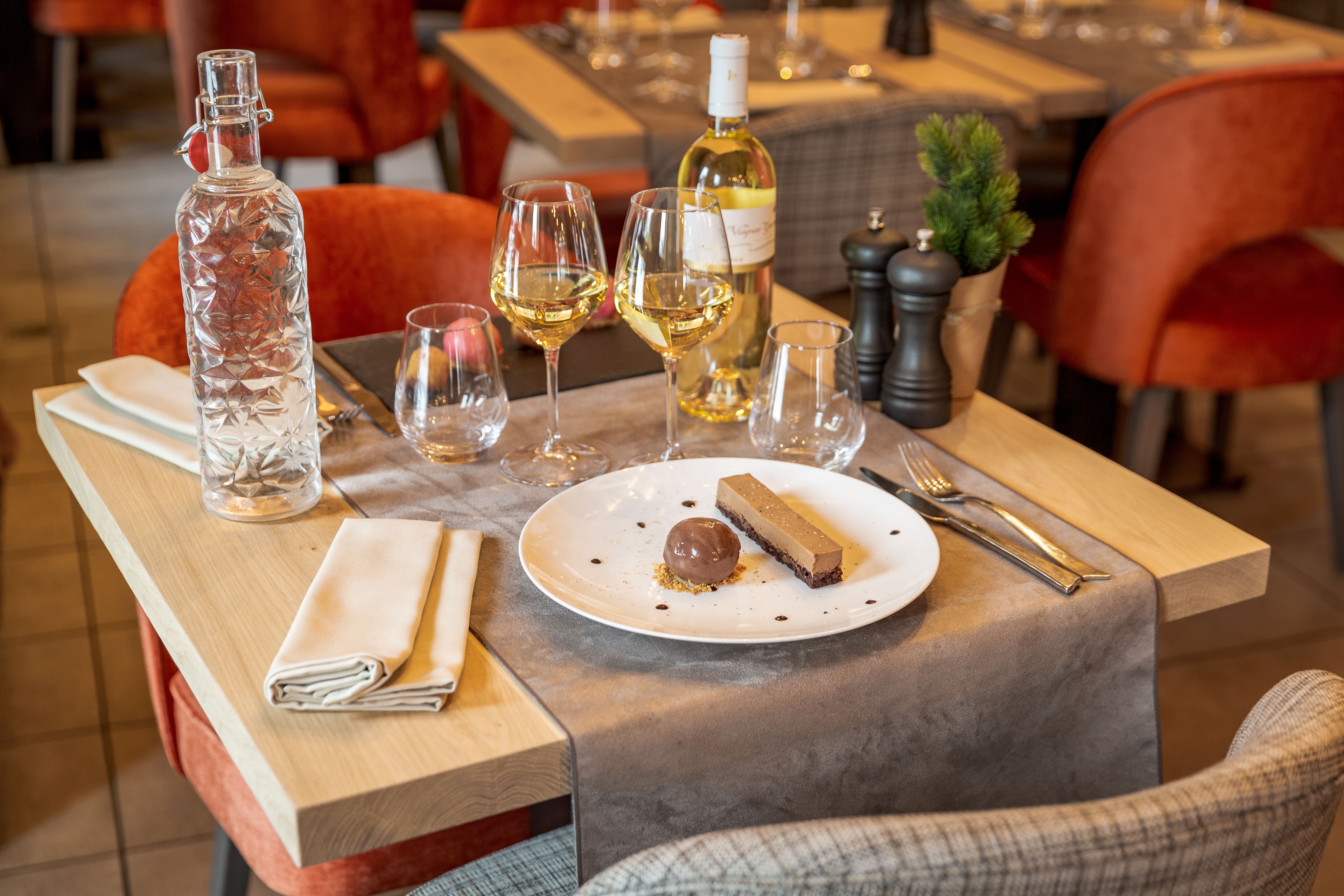 Una mesa de comedor con una botella, copas de vino, un plato de postre y cubiertos.