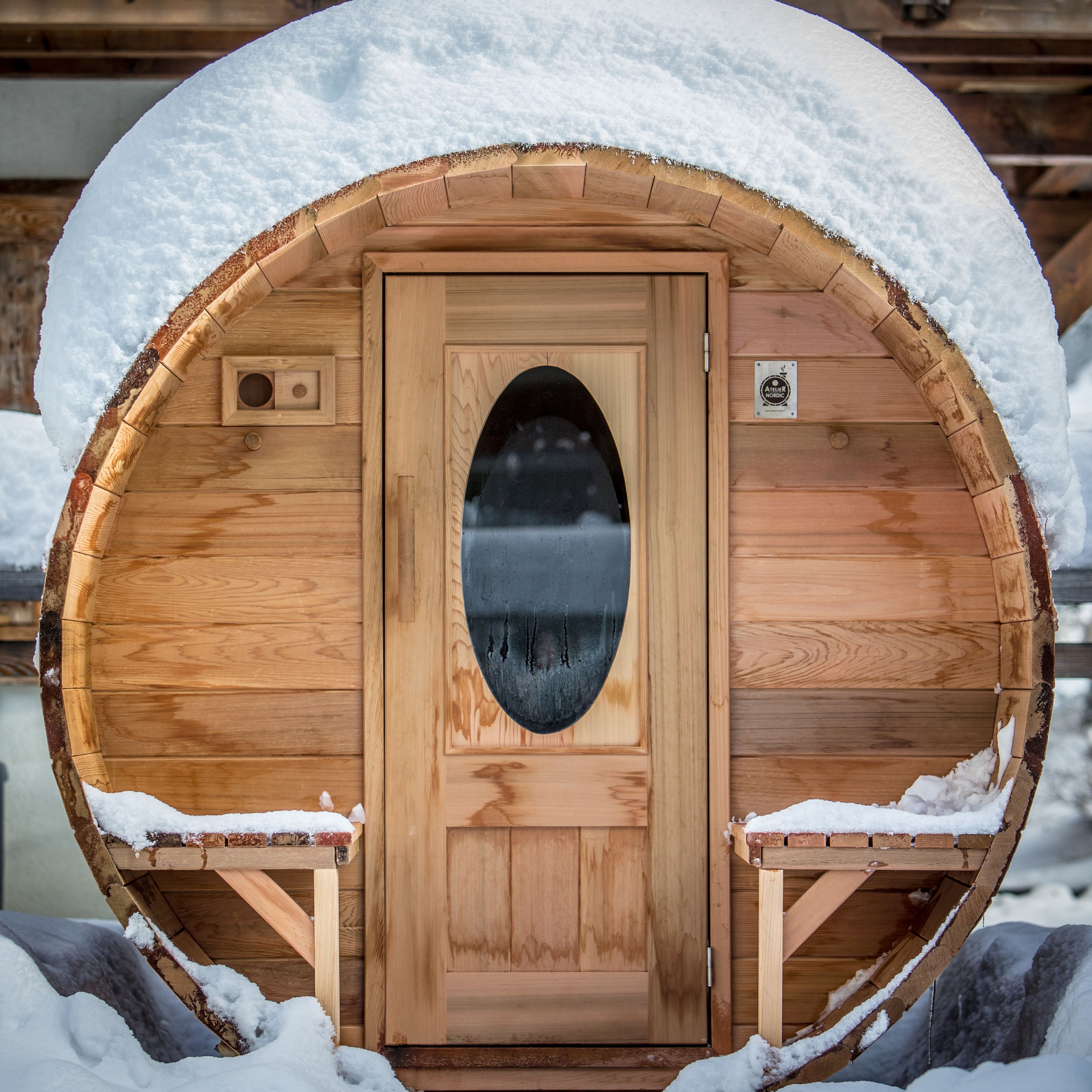 A wooden sauna with a circular shape and a central door, surrounded by snow.