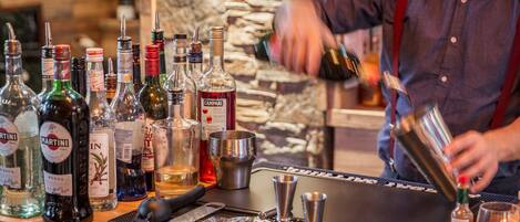 A bar area with various bottles of alcohol, a bartender preparing a drink, and bar tools on a counter.