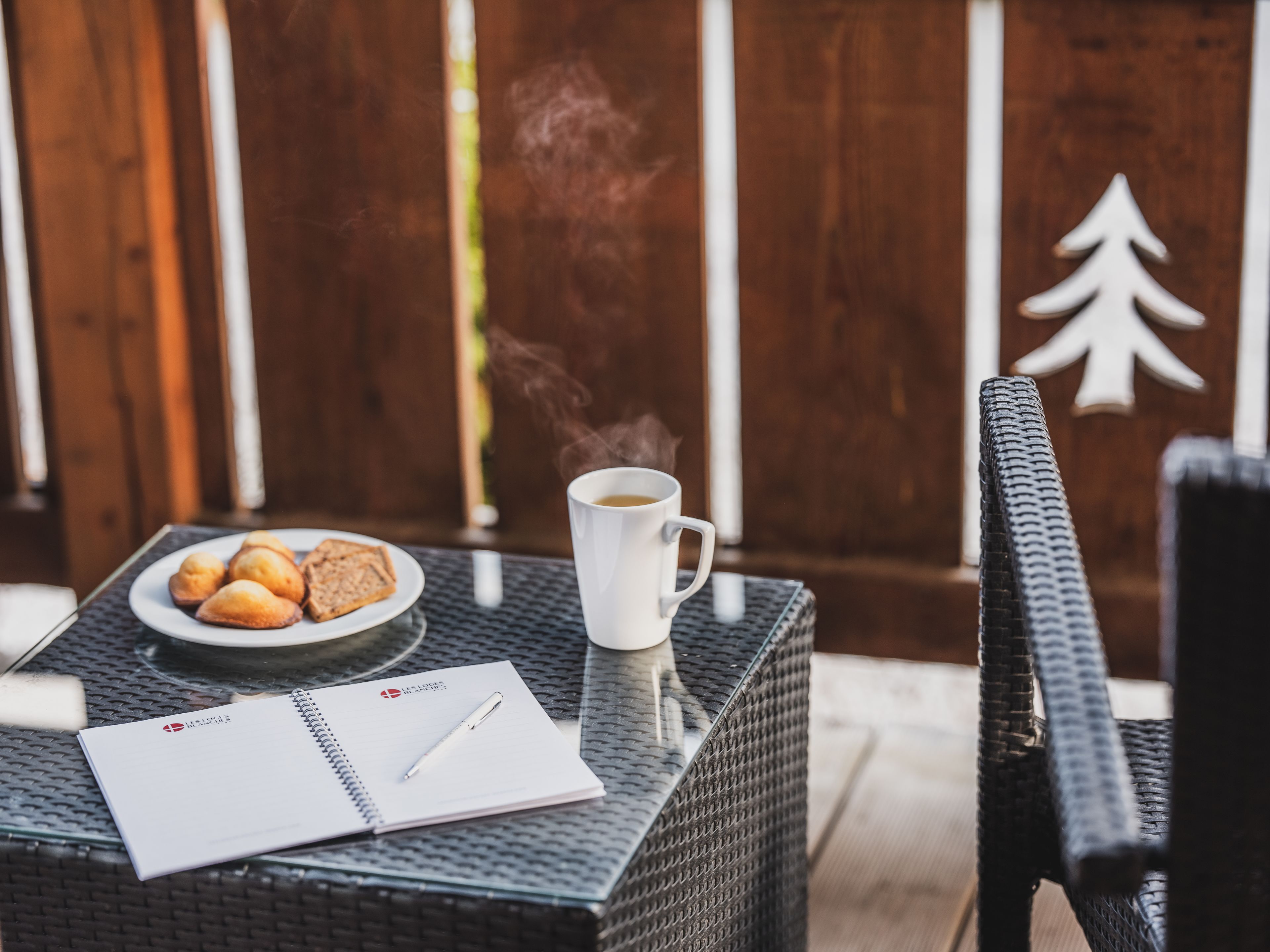 Una mesa con un plato de pasteles, una taza de café, un cuaderno y un bolígrafo.