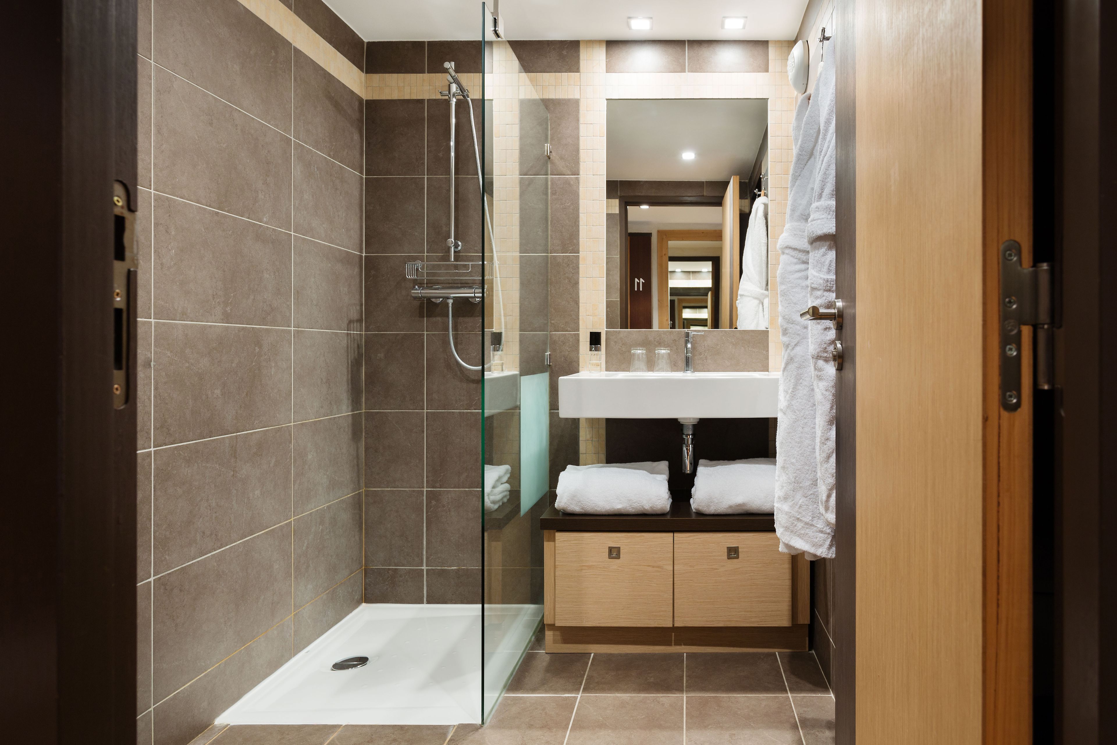 Un baño moderno con ducha envuelta en vidrio, tocador de madera con lavamanos y espejo arriba.