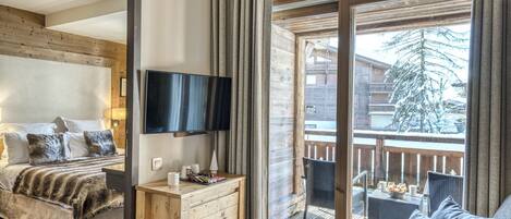 A hotel room with a bed, a TV, a wooden dresser, and a balcony with a view of a snowy landscape.