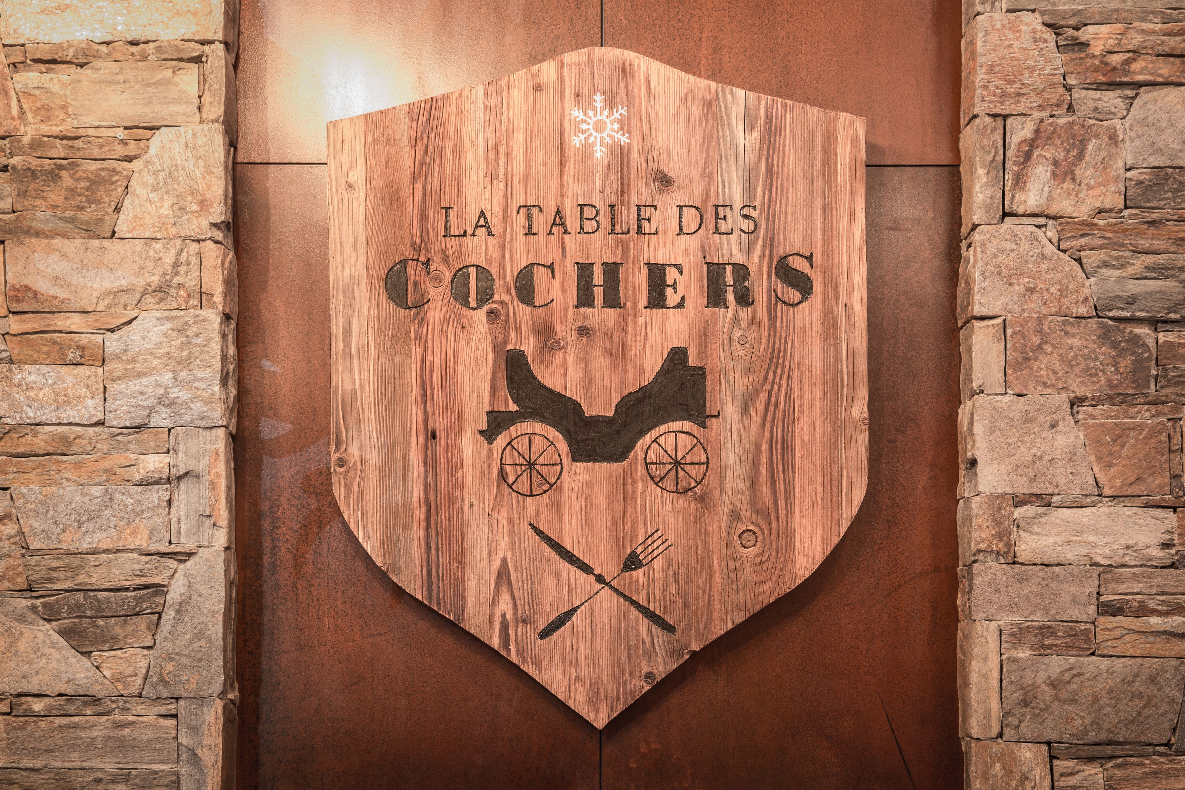 A wooden sign with the text "LA TABLE DES COCHERS" and a horse-drawn carriage illustration.