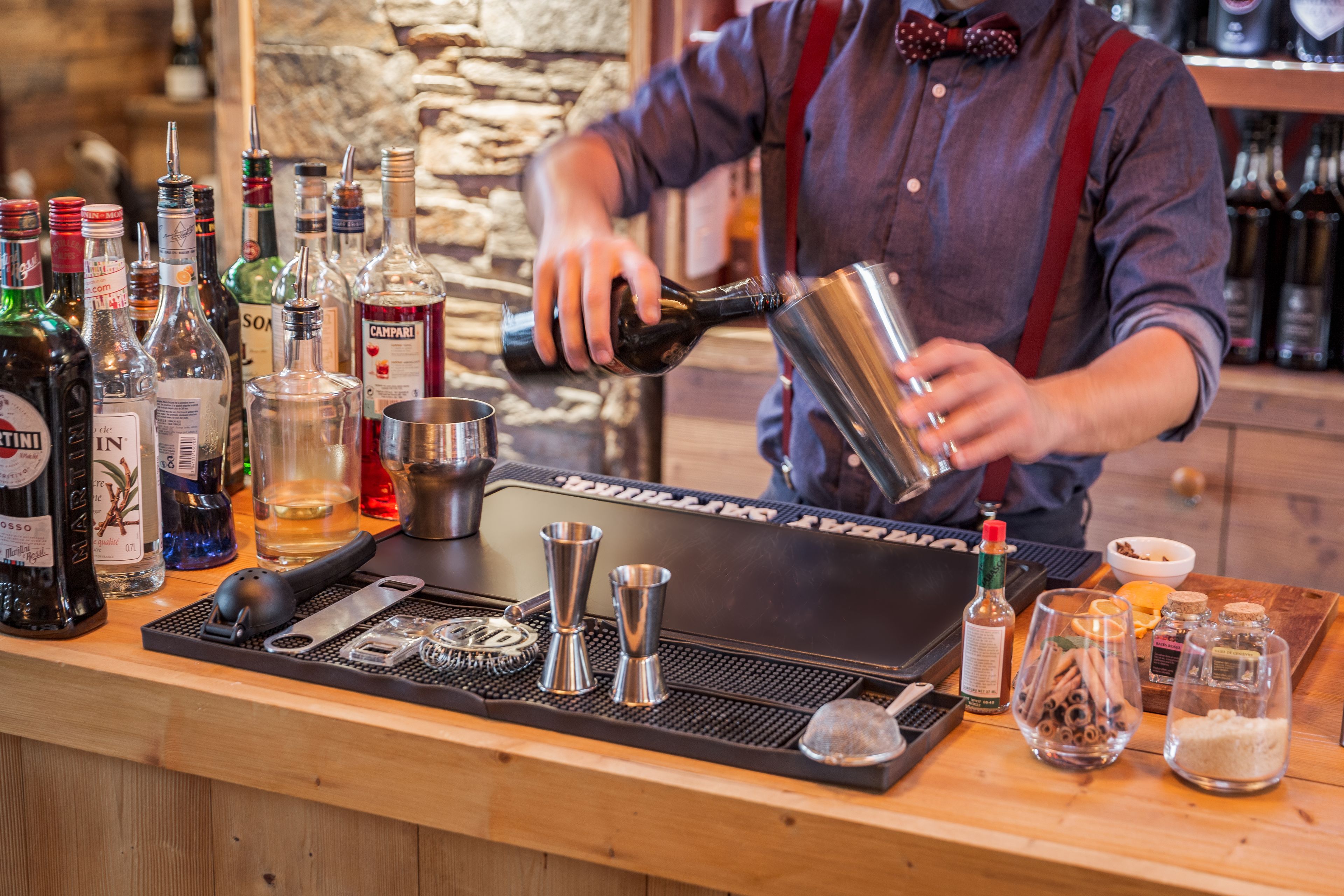 A bartender preparing a drink at a bar with various bottles and bar tools.