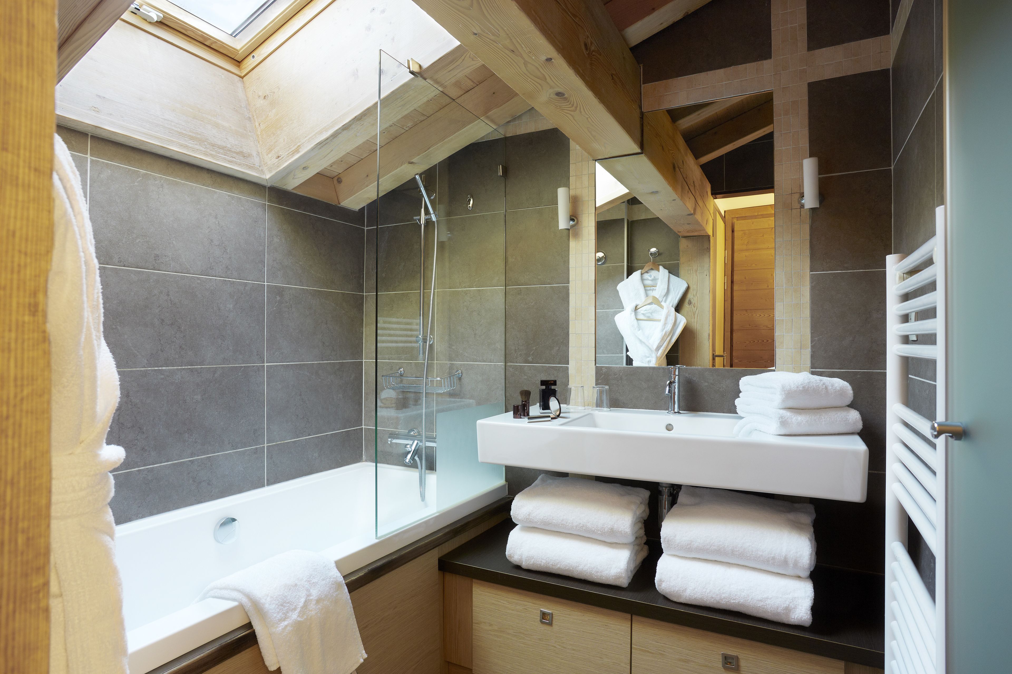 Une salle de bain moderne avec un puits de lumière, une douche en verre, un lavabo blanc et un porte-serviettes.