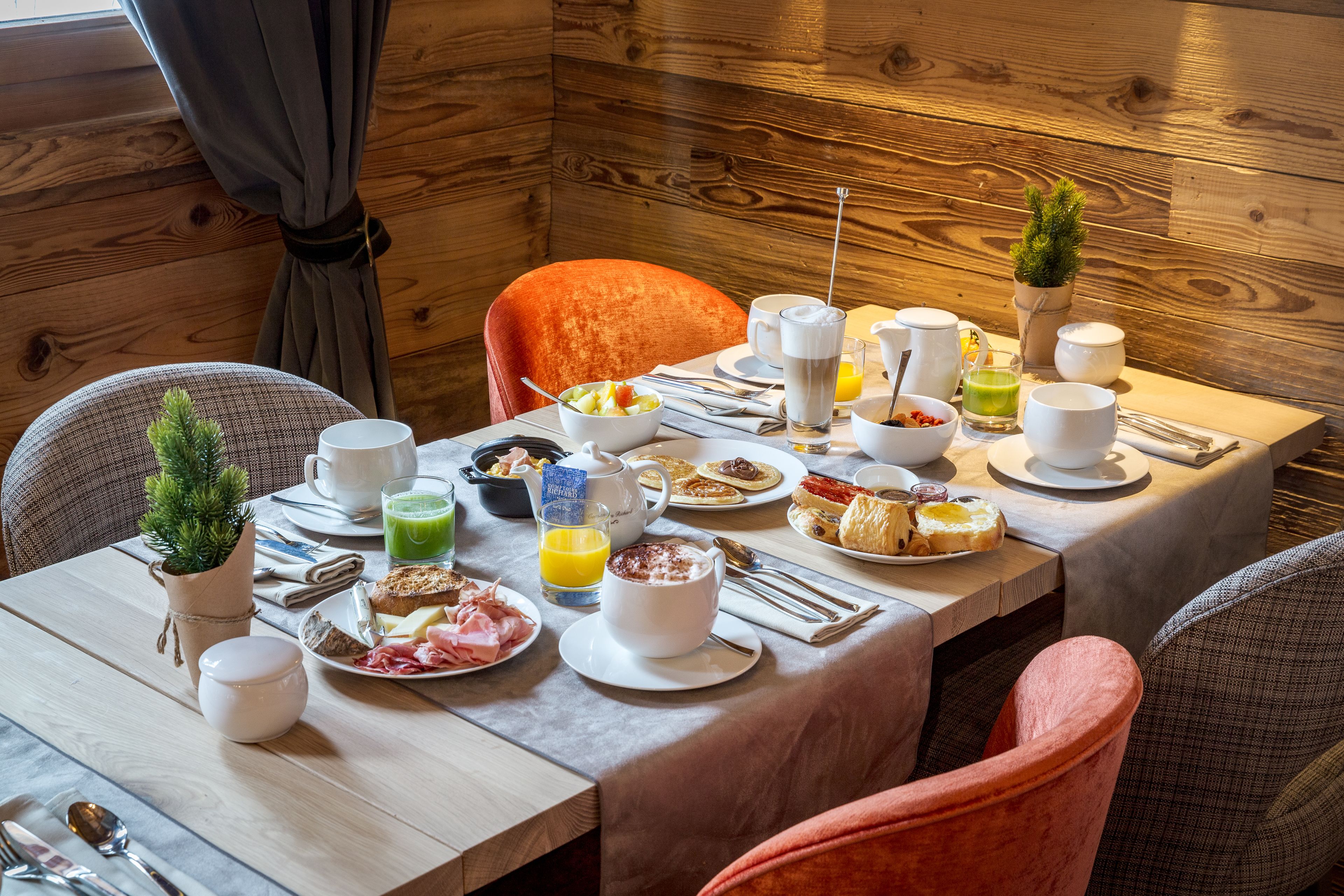 Habitación con paneles de madera y una mesa de desayuno preparada para dos personas, con platos de comida, tazas y una pequeña planta en maceta.