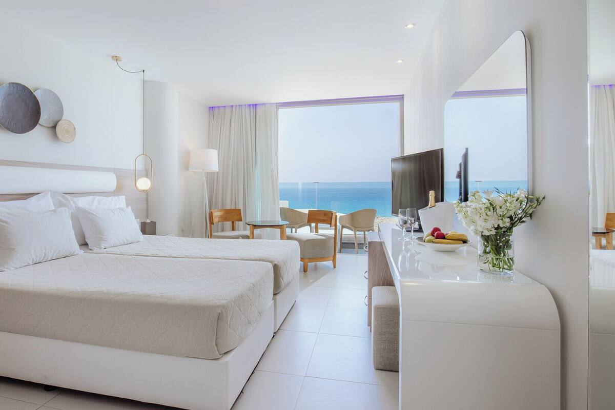 Une chambre d’hôtel avec deux lits, un bureau, une chaise, une télévision et une vue sur la mer.
