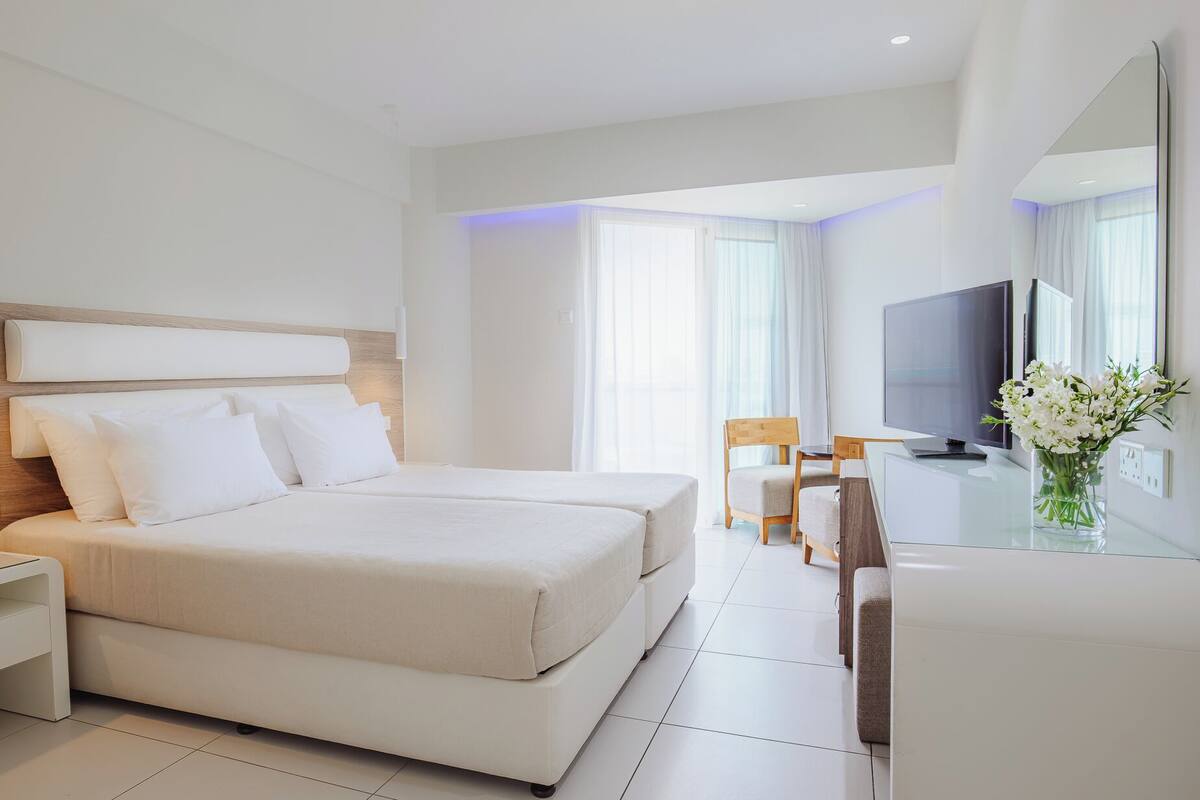 Une chambre d’hôtel moderne avec un grand lit, une table de chevet avec un téléphone, un bureau avec une chaise, une télévision et un vase de fleurs.