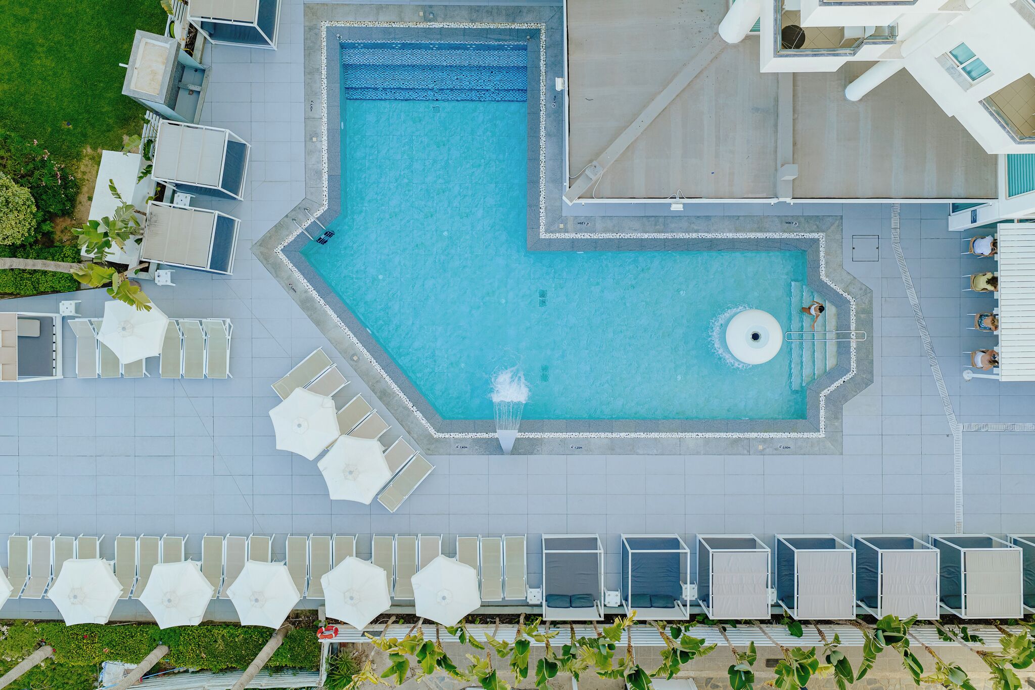 Piscina no terraço com um recurso de água azul cristalina, cercada por espreguiçadeiras e guarda-sóis.