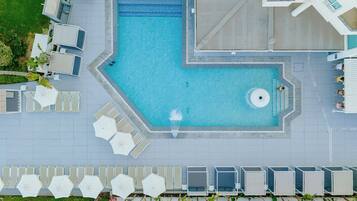 Piscina no terraço com um recurso de água azul cristalina, cercada por espreguiçadeiras e guarda-sóis.
