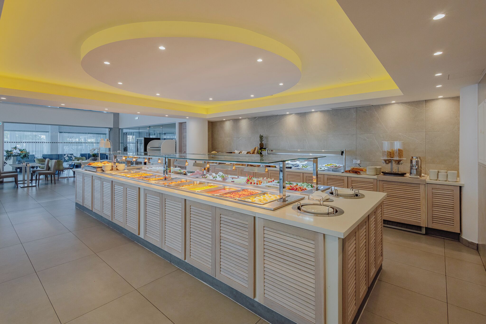 A modern breakfast bar with a variety of food options, a seating area with tables and chairs, and a large window providing natural light.