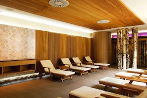 A spa area with wooden paneling, a row of sun loungers, and birch tree trunks as decor.