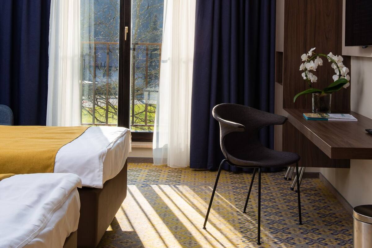 Ein Hotelzimmer mit Bett, Schreibtisch mit Stuhl, Fernseher und einem Fenster mit Vorhängen.