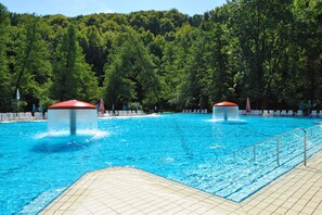 A swimming pool with two red water features, surrounded by a tiled deck and a forested hillside. - Hotel Šmarjeta - Terme Krka (Smarjeske Toplice)