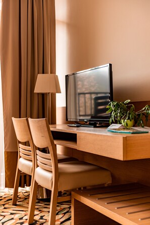 A hotel room with a wooden desk, a television, a lamp, two chairs, and a potted plant. - Hotel Šmarjeta - Terme Krka (Smarjeske Toplice)