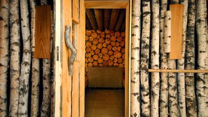 A room with birch bark walls, a wooden door, and a stack of logs in the background. - Hotel Šmarjeta - Terme Krka (Smarjeske Toplice)