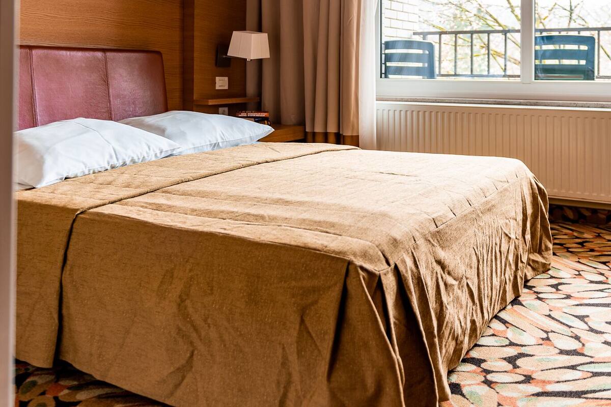 Ein Hotelzimmer mit einem großen Bett, einem Nachttisch, einer Lampe und einem Fenster mit Blick nach draußen.