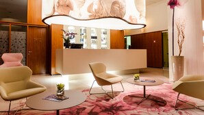 A modern reception area with a reception desk, two armchairs, a coffee table, and a large orchid plant. - Hotel Šmarjeta - Terme Krka (Smarjeske Toplice)