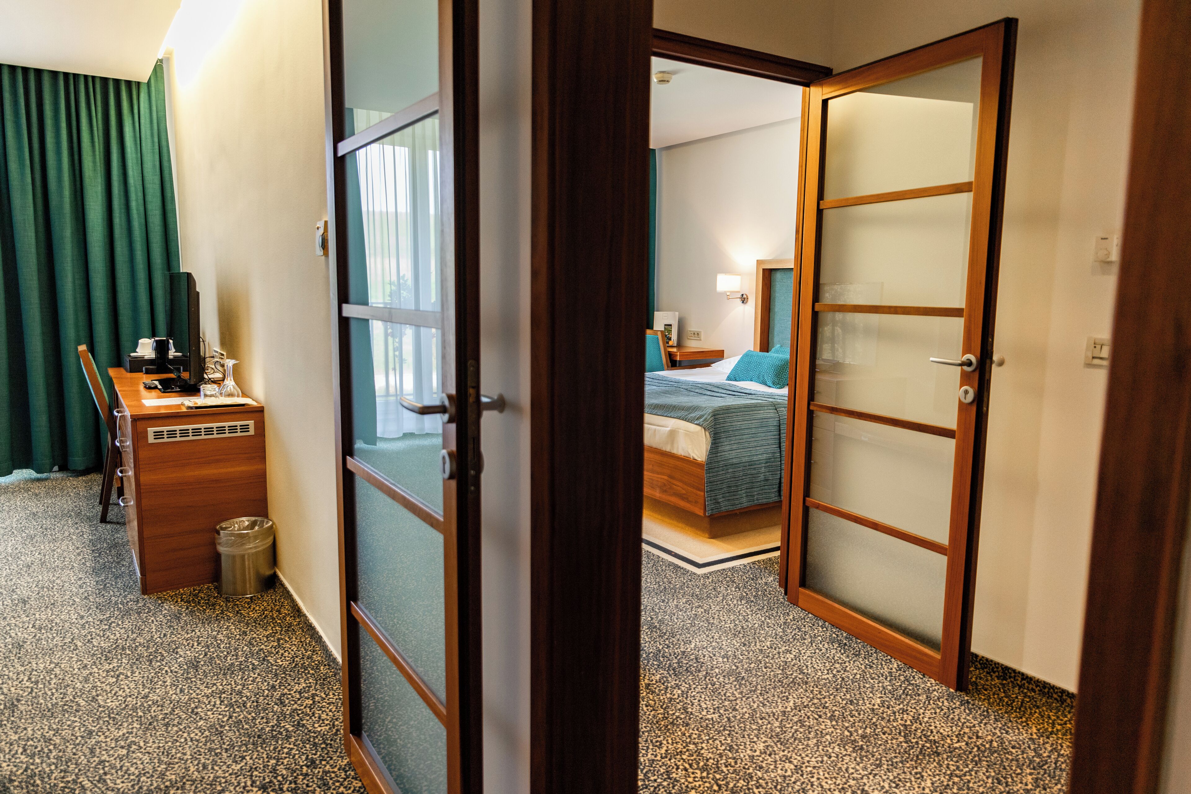 A hotel room with a desk, chair, and a bed with a green bedspread.