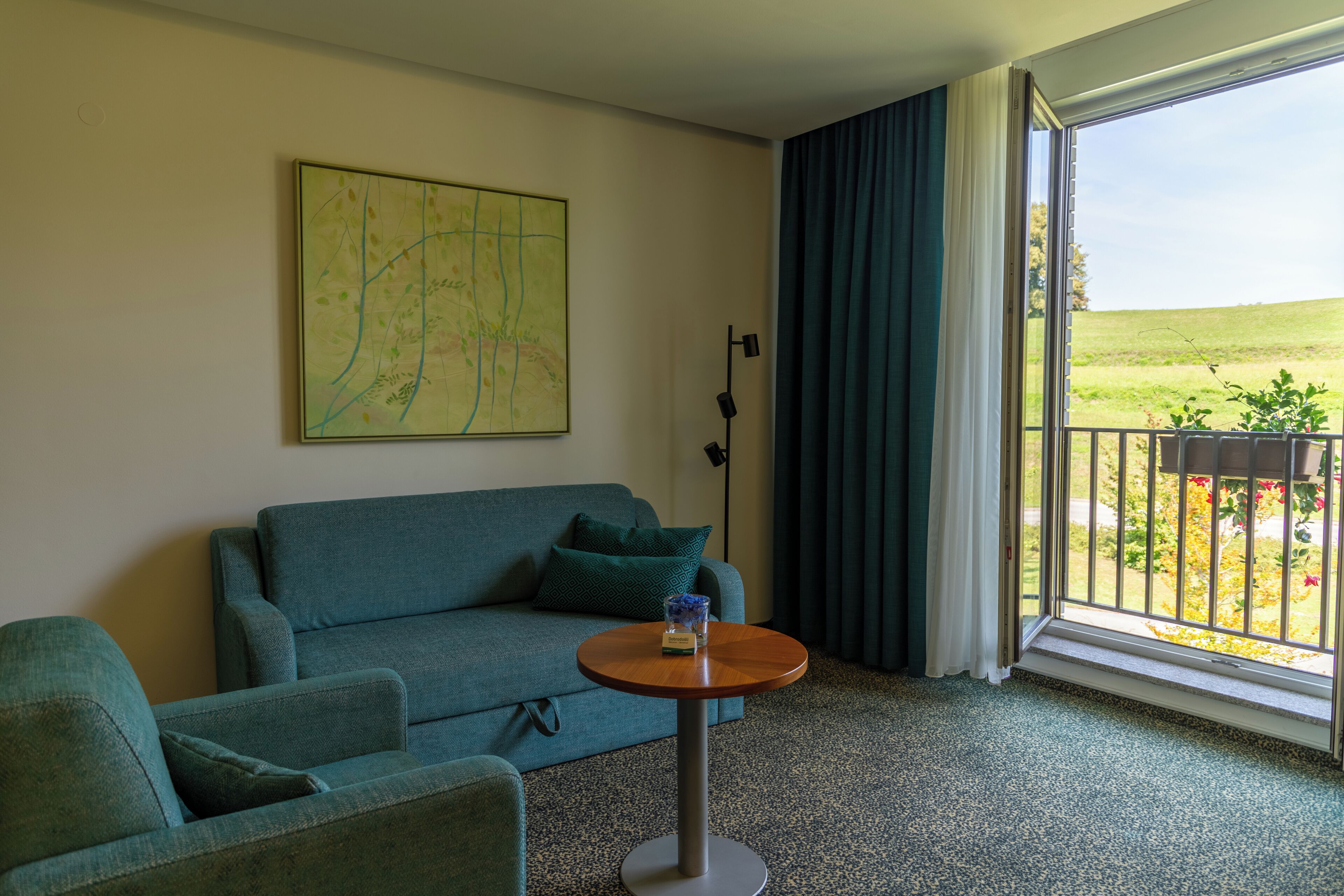Una habitación con sofá, una mesa redonda, un mapa en la pared y vistas de un jardín a través de una ventana.