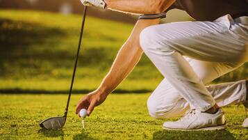 Une personne vêtue d’une chemise et d’un pantalon blancs, s’apprête à placer une balle de golf sur un support.