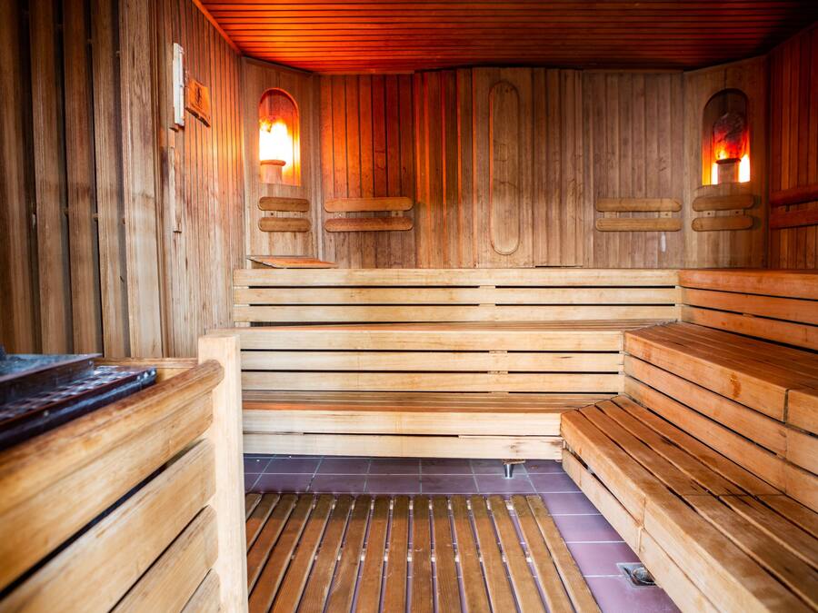 A wooden sauna with benches and two wall-mounted lights.