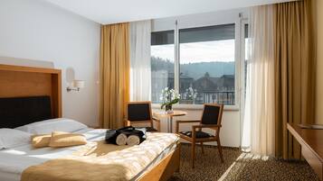 A hotel room with a bed, two chairs, a small table, and a window with curtains.